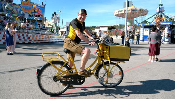 Wiesn-Zusteller Gerald Nadler mit dem Fahrrad vor einem Fahrgeschäft