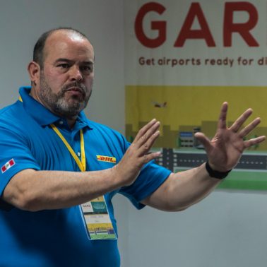 Ein DHL-Angestellter in einem blauen T-Shirt erklärt etwas. 