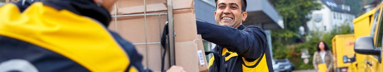 A DHL employee smiling as he pushes parcels in a wagon. 