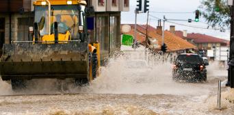 An excavator drives on a flooded road.