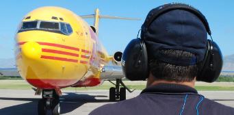 Ein Mann mit Gehörschutz schaut auf ein DHL Flugzeug.