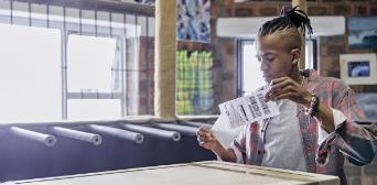 A young man with a ponytail in the process of putting a shipping label on a box.