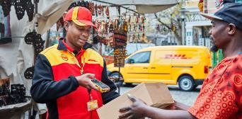 Ein DHL Zusteller scannt ein Paket. 