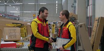 Two DHL employees shaking each other's hands in a warehouse.