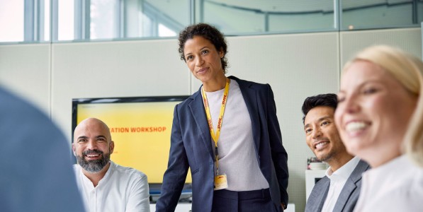 Three sitting employees and one standing up in a DHL conference room.