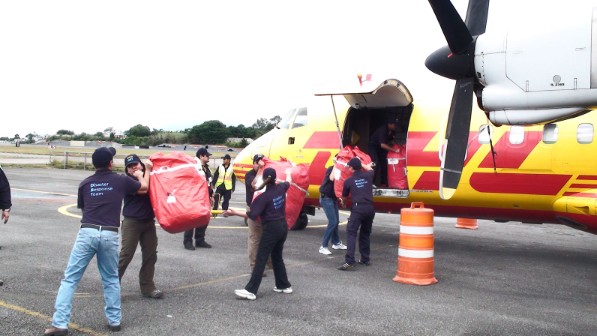 Eine Gruppe Menschen belädt ein Flugzeug mit roten Beuteln. 