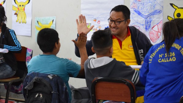 Ein Mann in einem DHL T-Shirt gibt einem Jungen in einem Klassenzimmer einen High-five. 