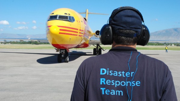 A man with cap and ear protection in front of a plane.