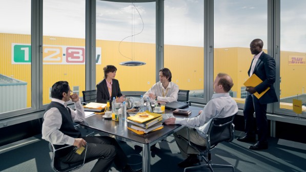 A group of employees sitting in a conference room in front of a DHL warehouse.