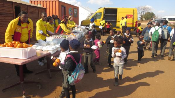 DHL volunteers giving out food to children in front of a DHL van.