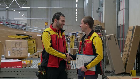 Two DHL employees shaking each other's hand in a sorting facility.