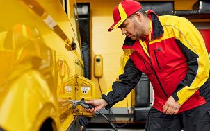 Eine Kachel mit einem der 2030 Ziele und ein Mann in DHL-Kleidung, der sein Elektrofahrzeug auflädt. 